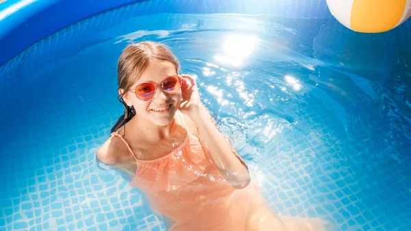 Portrait of cheerful smiling girl relaxing and splashing water in swimming pool on hot summer day. Concept of happy and cheerful summer holidays and vacation — Stock Photo, Image