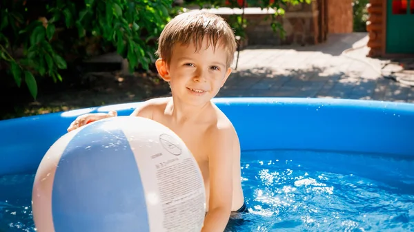 Buon bambino sorridente playin con grande palla da spiaggia colorata nella piscina gonfiabile nel giardino del cortile della casa. Concetto di vacanze estive felici e allegre e vacanze — Foto Stock