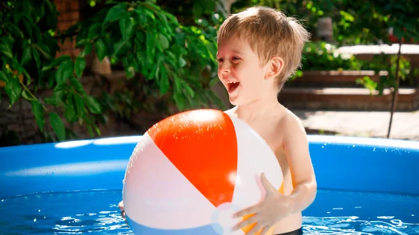 Ritratto di ragazzo carino di 5 anni che gioca con pallone da spiaggia gonfiabile nella piscina all'aperto. Concetto di vacanze estive felici e allegre e vacanze — Foto Stock