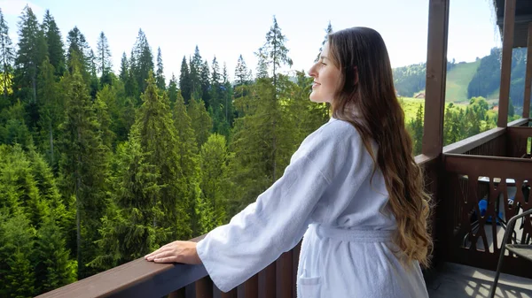 Retrato de una mujer sonriente en albornoz disfrutando de la vista de las montañas desde su habitación de hotel. Concepto de turismo y vacaciones en las montañas en verano —  Fotos de Stock