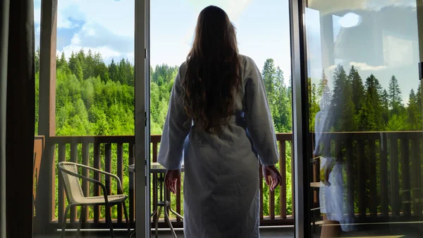 Giovane donna in accappatoio che esce dalla camera d'albergo sulla terrazza e tende le mani. Concetto di turismo e vacanza in montagna in estate — Foto Stock