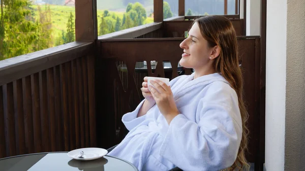 Sluiten van mooie brunette vrouw drinken koffie in de ochtend en kijken op dennenbos. Concept van mensen reizen, toerisme en vakantie in de bergen in de zomer — Stockfoto