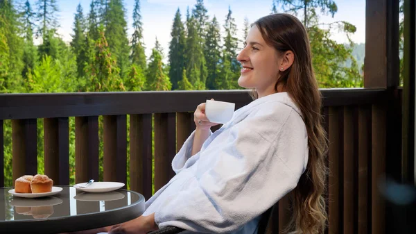 Mujer sonriente bebiendo té y mirando a la montaña desde su habitación de hotel. Concepto de personas viajando, turismo y vacaciones en las montañas en verano —  Fotos de Stock