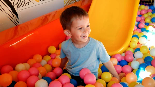子供の遊び場でスライドに乗って子供たちを笑って、カラフルなプラスチックボールでプールでダイビング. — ストック写真