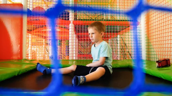 Upprörd liten pojke känner sig ledsen när du spelar på lekplatsen med studsmatta. — Stockfoto