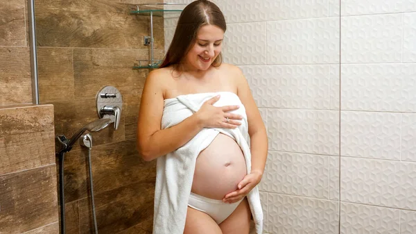 Glad leende gravid kvinna smeka och röra hennes växande mage i badrummet. Begreppet kvinnlig skönhet, kroppsvård och hälsovård under graviditeten. — Stockfoto