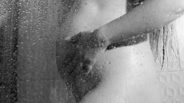 Czarno-biały obraz seksownej kobiety w ciąży myjącej i relaksującej się pod prysznicem za szklanymi drzwiami. Pojęcie kobiecej urody, pielęgnacji ciała i opieki zdrowotnej w czasie ciąży. — Zdjęcie stockowe