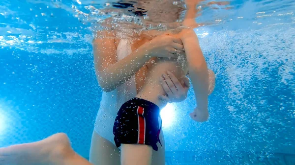 Su altında, küçük oğlunu destekleyen ve yüzme havuzunda yüzmeyi öğrenen genç bir anneyi vurdu. Aile sağlık ve spor anlayışı. — Stok fotoğraf