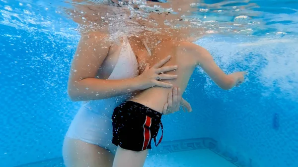 Unterwasseraufnahmen einer jungen Mutter, die ihren kleinen Sohn beim Schwimmen im Schwimmbad unterstützt. Konzept der Familiengesundheit und des Sports. — Stockfoto