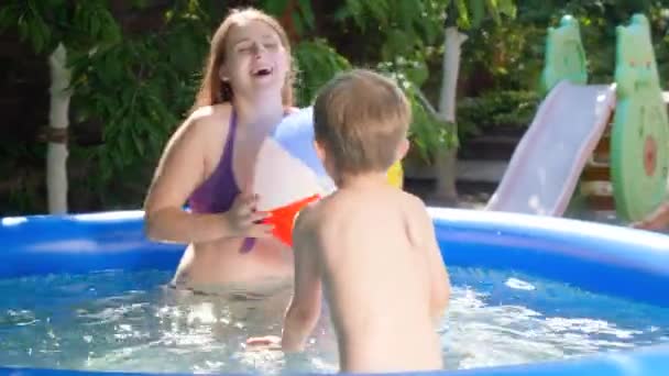 Glücklich lächelnde Mutter mit kleinem Jungen, der im aufblasbaren Swimmingpool auf dem Hinterhof des Hauses mit Beachball spielt. Sommerurlaub und Urlaub für Familien — Stockvideo