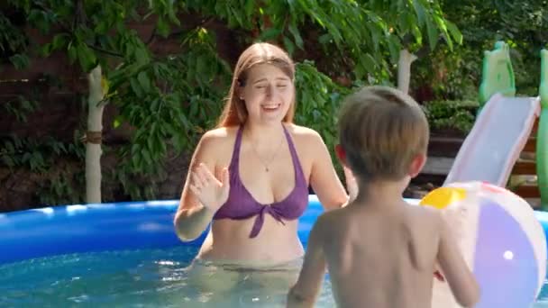 Mutlu gülen anne ve küçük oğlu yüzme havuzunda renkli plaj topuyla oynuyorlar. Aile yaz tatili ve tatiller — Stok video