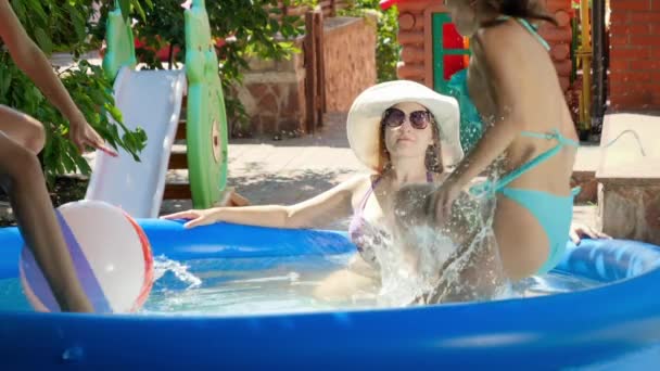 İki genç kız suya atlayıp su sıçratırken şapkalı genç bir kadının havuzda dinlenme hareketi. Aile yaz tatili ve tatiller — Stok video