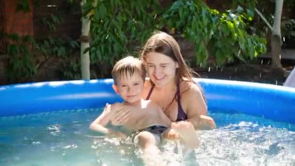 Glücklich lächelnde Mutter hält und stützt ihren kleinen Sohn, der im aufblasbaren Schwimmbad schwimmen lernt. Sommerurlaub und Urlaub für Familien — Stockvideo