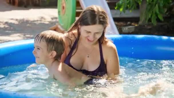 Zeitlupe einer jungen lächelnden Mutter, die an einem sonnigen Sommertag ihr kleines Schwimmbad hält und stützt. Familie mit Kindern Sommerurlaub und Urlaub — Stockvideo