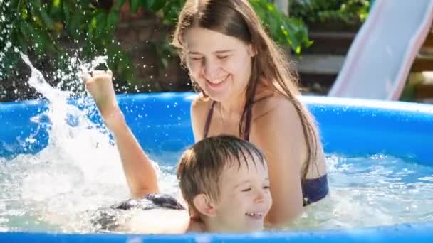 Movimiento lento de niño riendo salpicaduras de agua mientras aprende a nadar en la piscina al aire libre con la madre joven. Familia con niños vacaciones de verano y vacaciones — Vídeos de Stock