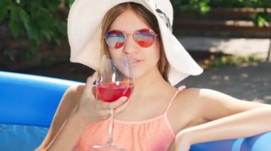 Sıcak yaz günlerinde yüzme havuzunda dinlenirken kokteyl içen güzel bir kızın portresi. Mutlu yaz tatilleri ve tatil kavramı