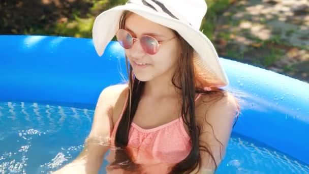 Portrait de jeune fille souriante en chapeau d'été et lunettes de soleil relaxantes dans la piscine extérieure. Vacances d'été et vacances — Video