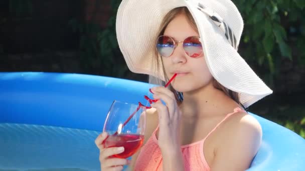 Счастливая улыбающаяся молодая женщина пьет коктейль из соломы, отдыхая в бассейне. Концепция счастливых летних каникул и каникул — стоковое видео