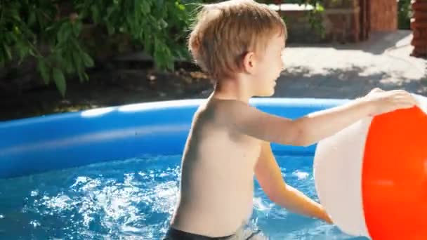 Brincadeira de menino sorridente feliz com grande bola de praia colorida na piscina inflável no jardim do quintal da casa. Conceito de férias de verão felizes e alegres e férias — Vídeo de Stock