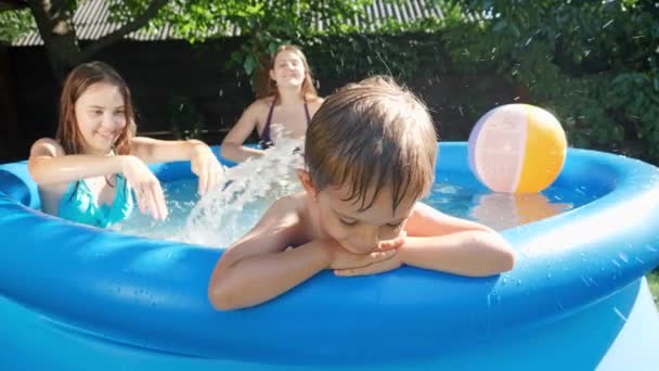 Porträt eines aufgebrachten kleinen Jungen, der am Pool sitzt, während die Familie spielt und Spaß hat. Konzept für fröhliche und fröhliche Sommerferien und Urlaub — Stockvideo