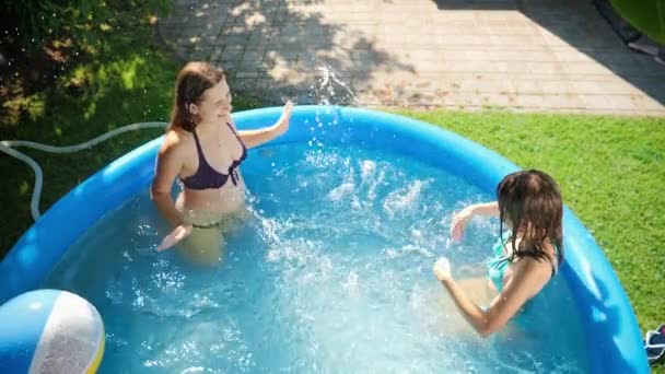 Mutlu gülümseyen anne ve su sıçratan kız ve şişme açık havuzda oynuyorlar. Mutlu ve neşeli yaz tatili ve tatil kavramı — Stok video