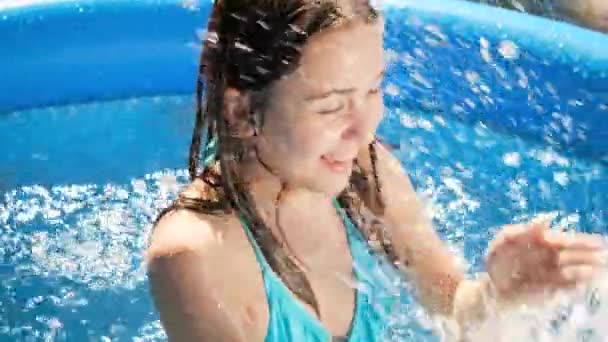 Retrato de la feliz risita salpicando agua y jugando en traje de baño en la piscina al aire libre. Concepto de felices y alegres vacaciones familiares de verano y vacaciones — Vídeos de Stock