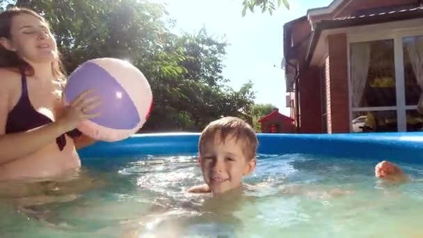 Портрет счастливого веселого мальчика, веселящегося в бассейне с семьей, играющей в пляжный волейбол. Концепция счастливых и веселых семейных летних каникул и каникул — стоковое видео