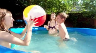 Kumsal topuyla oynayan mutlu bir ailenin yüzme havuzunda rahatlarken birbirlerine attığı yavaş çekim. Mutlu ve neşeli aile kavramı yaz tatili ve tatil