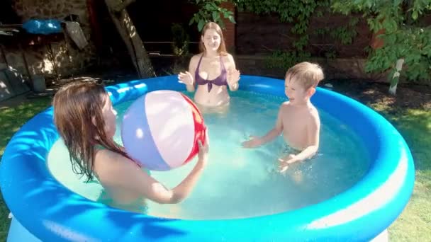 Muchacho divertido jugando con la bola colorida inflable en la piscina en el jardín trasero de la casa. Concepto de felices y alegres vacaciones familiares de verano y vacaciones — Vídeos de Stock