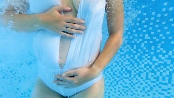 Підводний знімок красивої вагітної жінки в купальнику, що розслабляється в басейні і погладжує живіт. Концепція охорони здоров'я та спорту вагітності — стокове відео
