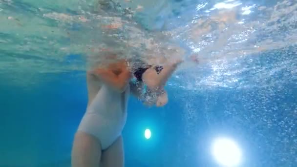 Underwater shot of young mother holding and spinning her little boy in inflatable ring at swimming pool — Stock Video