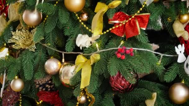 Panning close-up shot van mooie versierde kerstboom met veel kerstballen, lichte bloemenslingers en linten. Wintervakantie achtergrond of achtergrond. — Stockvideo