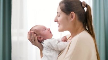 Mutlu gülümseyen annenin yakın plan portresi kucağında ve yeni doğmuş bebeğine bakıyor. Aile mutluluğu ve küçük çocuklu sevgi dolu ebeveynler.