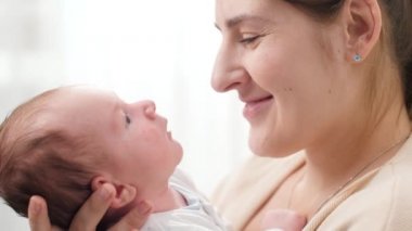 Yeni doğmuş bebeğiyle gülümseyen bir annenin yakın plan portresi büyük parlak bir pencerenin önünde. Aile mutluluğu ve küçük çocuklu sevgi dolu ebeveynler.