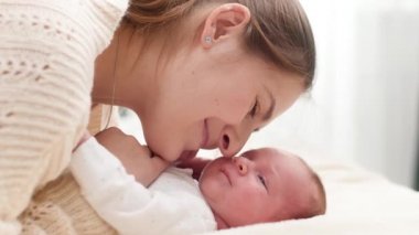Sevimli, gülümseyen yeni doğmuş bebeğin portresi ve yatak odasındaki büyük pencerenin önünde yatan mutlu genç anne. Aile mutluluğu ve küçük çocuklu sevgi dolu ebeveynler.