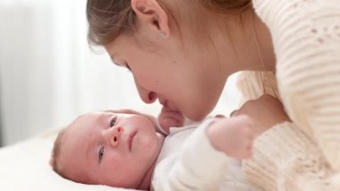 Sevimli yeni doğmuş erkek bebek güneşli bir sabahta büyük bir pencereye karşı genç annesiyle birlikte yatakta yatıyor. Aile mutluluğu ve küçük çocuklu sevgi dolu ebeveynler.