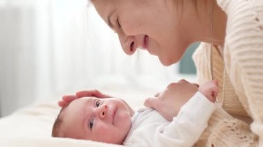 Sevgi dolu bir annenin gülümseyen portresi ve güneşli bir günde yeni doğmuş bebeğini yatakta yatarken izlemek. Aile mutluluğu ve küçük çocuklu sevgi dolu ebeveynler.