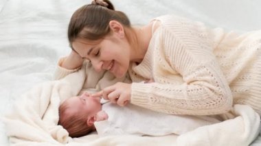 Gülümseyen mutlu bir annenin 1 aylık bebeğini yatakta oynatıp gıdıkladığı yavaş çekim. Aile mutluluğu ve küçük çocuklu sevgi dolu ebeveynler.