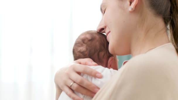 Primer plano de la joven madre cariñosa abrazando a su bebé recién nacido y apoyando su cabeza con la mano. Concepto de felicidad familiar y padres amorosos con niños pequeños — Vídeo de stock