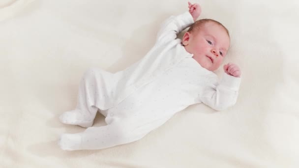 Vista superior de adorable bebé recién nacido en traje de cuerpo blanco acostado en la cama y mirando el sol brillante. Bebés recién nacidos en casa — Vídeo de stock