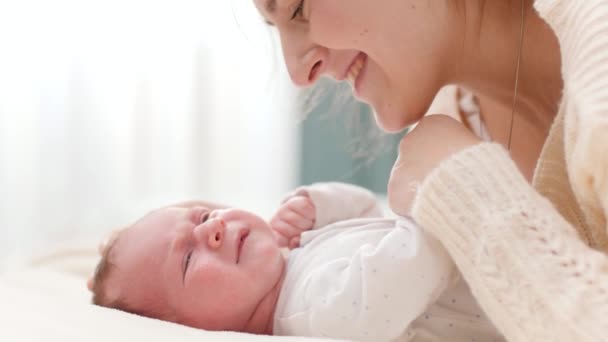 Seitenansicht Porträt einer glücklich lächelnden Mutter, die ihr Neugeborenes streichelt und kuschelt, das auf dem Bett liegt. Konzept des Familienglücks und liebevoller Eltern mit kleinen Kindern — Stockvideo