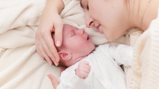 Nahaufnahme eines kleinen Neugeborenen, das neben der Mutter liegt und weint. Glücklich lächelnde Frau mit Blick auf ihr kleines Kind. Konzept des Familienglücks und liebevoller Eltern mit kleinen Kindern — Stockvideo