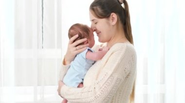 Mutlu, gülümseyen bir annenin portresi. Yeni doğmuş bebeğini büyük bir pencereden seyrediyor. Aile mutluluğu ve küçük çocuklu sevgi dolu ebeveynler..