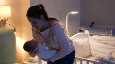Güzel gülümseyen anne gece yatak odasında yeni doğmuş bebeğini kucaklıyor. Annem elbiselerini küçük bir çocukla değiştiriyor. Sevgi ve şefkat kavramı, yeni doğmuş bebekler ve aile