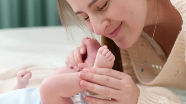 Porträt einer glücklichen liebenden Mutter, die kleine Babyfüße küsst und in der Krippe hält. Konzept des Familienglücks und liebevoller Eltern mit kleinen Kindern — Stockvideo