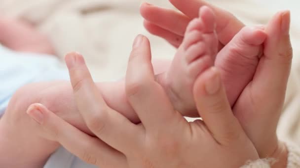 Primo piano della giovane madre che stringe delicatamente e tocca i piedini del suo neonato sdraiato sul letto. Concetto di felicità familiare e genitori amorevoli con bambini piccoli — Video Stock