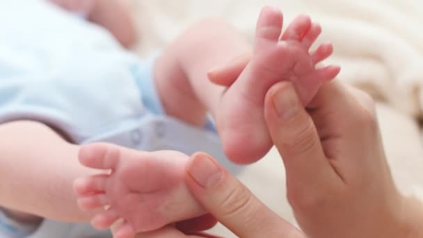 Primo piano della giovane madre premurosa e amorevole massaggiando e accarezzando i piedini del suo neonato sdraiato a letto. Concetto di felicità familiare e genitori amorevoli con bambini piccoli. Massaggio per bambini e — Video Stock