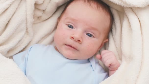 Porträt von oben: 1 Monate altes Baby mit blauen Augen liegt auf weißer weicher Decke auf dem Bett und blickt in die Kamera. — Stockvideo