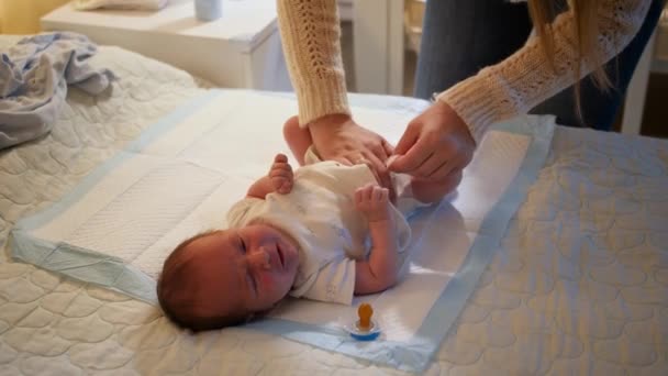 Giovane madre che cambia pannolini disordinati al suo neonato che piange sul letto di notte. Concetto di igiene del bambino, genitori amorevoli e premurosi e felicità familiare. — Video Stock