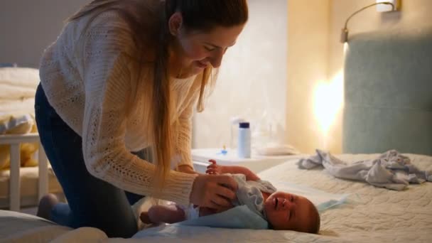 Pequeno bebê recém-nascido chorando e gritando enquanto a mãe troca de roupa e fraldas na cama à noite. Conceito de higiene do bebê, pais amorosos e carinhosos e felicidade familiar. — Vídeo de Stock